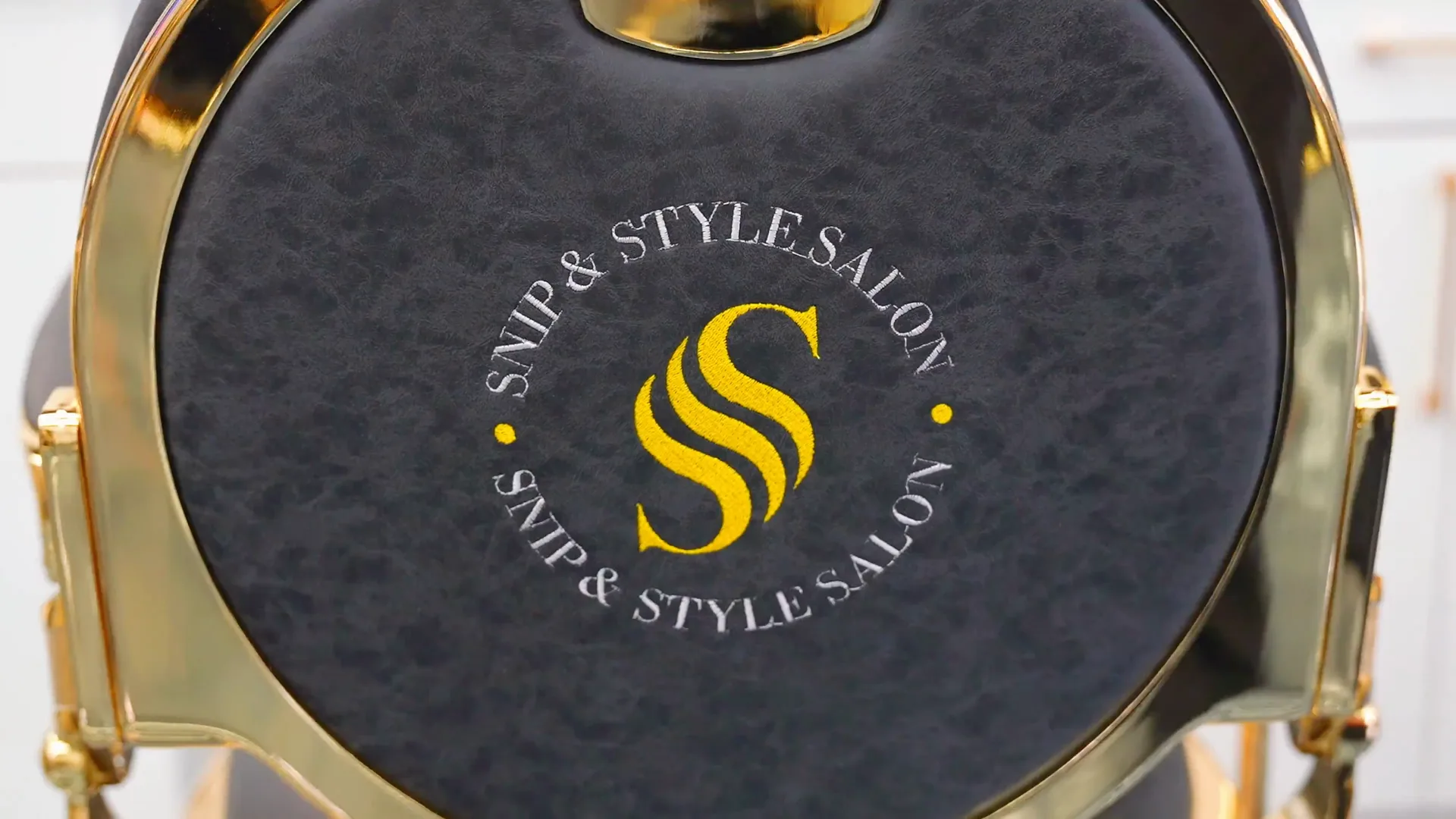 Detail of a styling chair back carrying the Snip & Style logo, with the resin floor reflecting the ceiling lighting behind it.