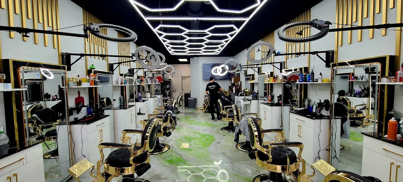 The finished salon looking down the room — gold styling chairs either side, a lit mirror and ring light at every station, and a hexagon LED grid across the black ceiling.