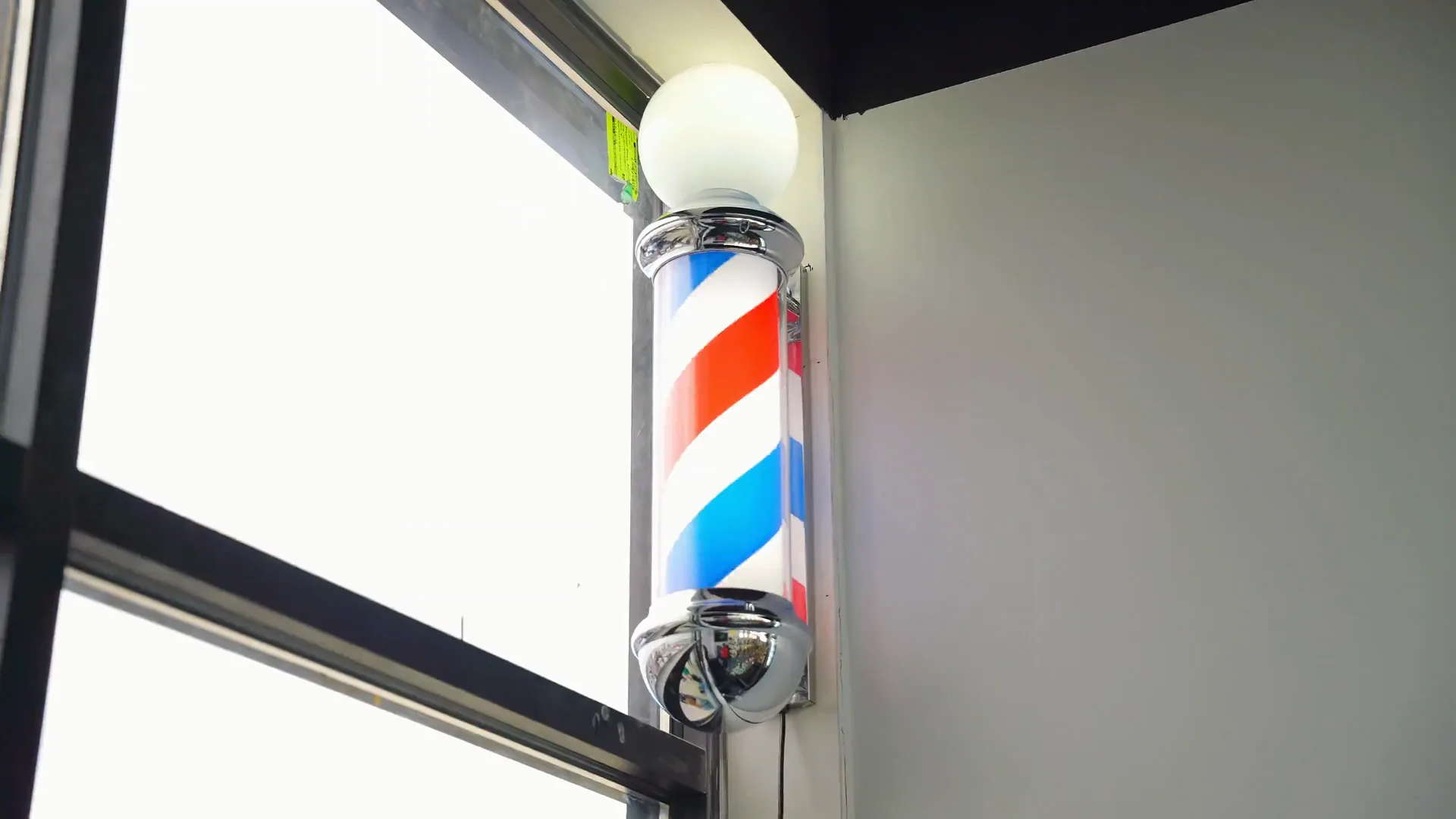 A traditional barber pole mounted by the shopfront glazing at the entrance.