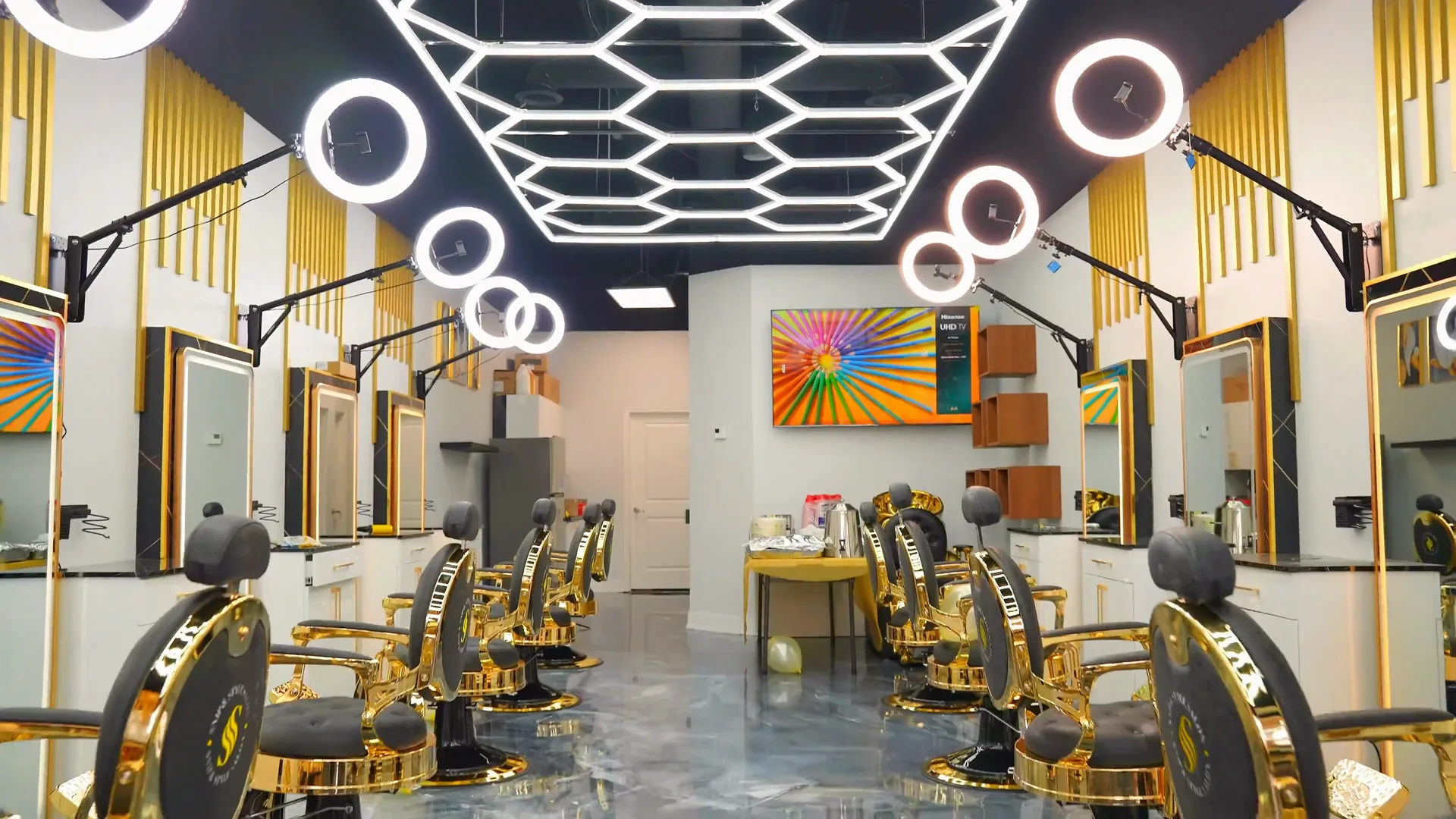 Styling stations along one wall, with fluted gold wall panelling, retail display shelving and branded capes at each chair.